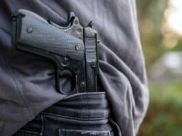 Gloved hand carrying a pistol in his pants, blur nature background,